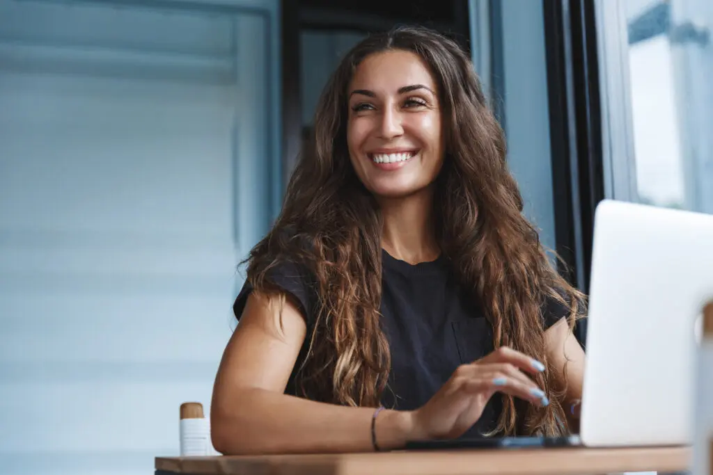 Girl with long wavy hair in front of laptop smiling